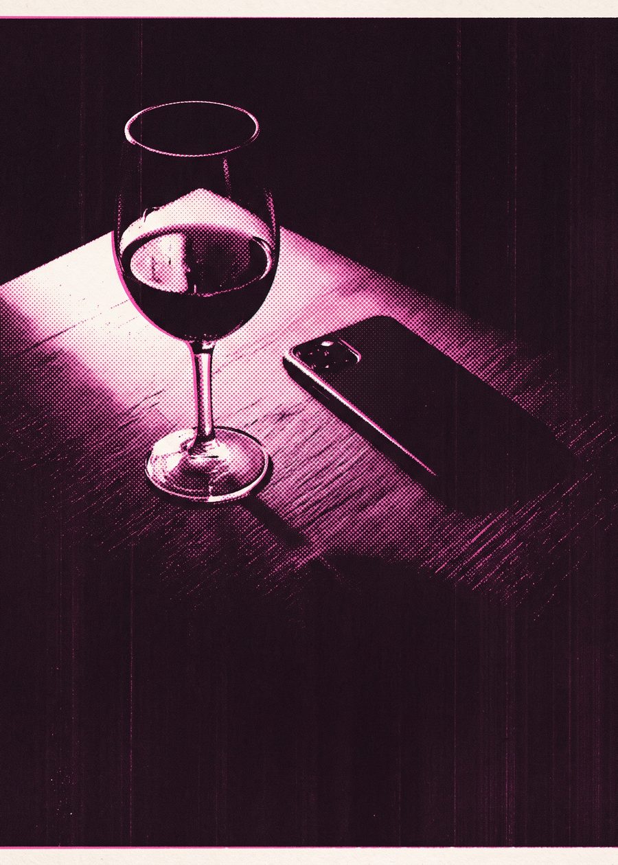 a half-finished glass of red wine beside a phone lying face-down on a wooden table